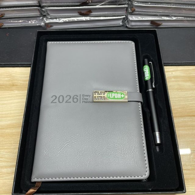 Grey 2026 planner with a branded metal clasp and matching pen, presented in a black gift box.