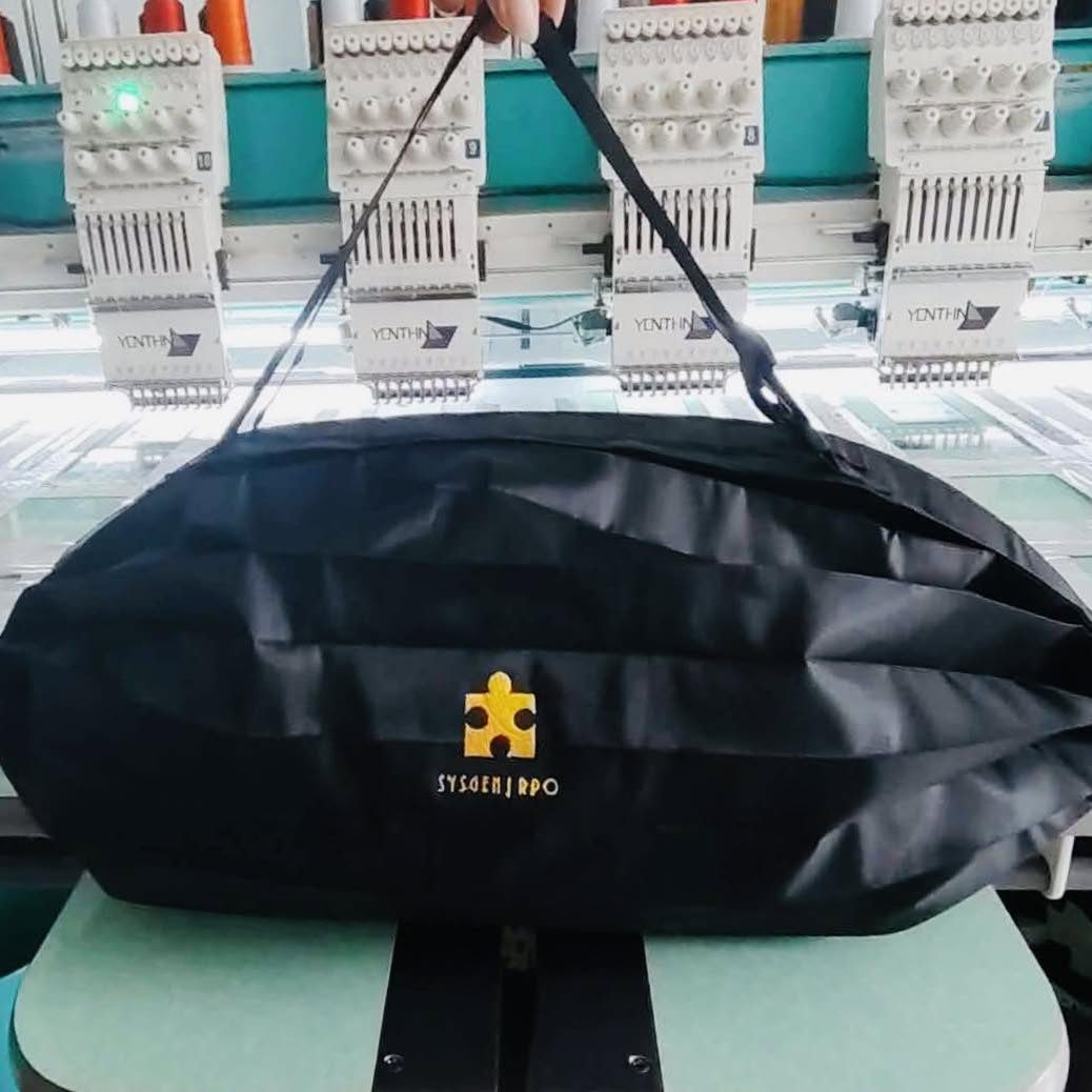 A corporate duffel bag on a multi-head embroidery machine, mid-production, with the client logo stitched in gold thread.